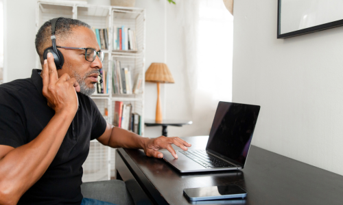 Infinity Tech Consulting professional wearing headphones conducting video call on laptop in modern home office setting